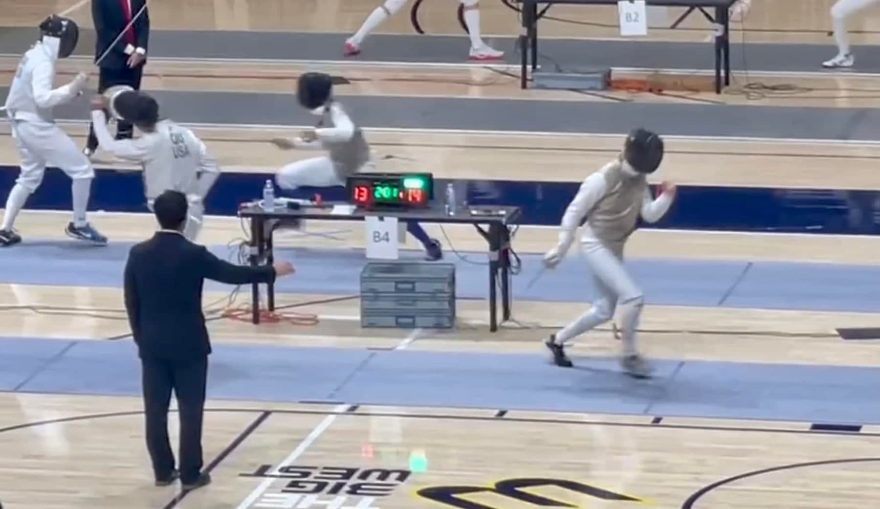 Marin Fencing Academy — A fencer attacking down the strip at a large tournament venue, referee alongside