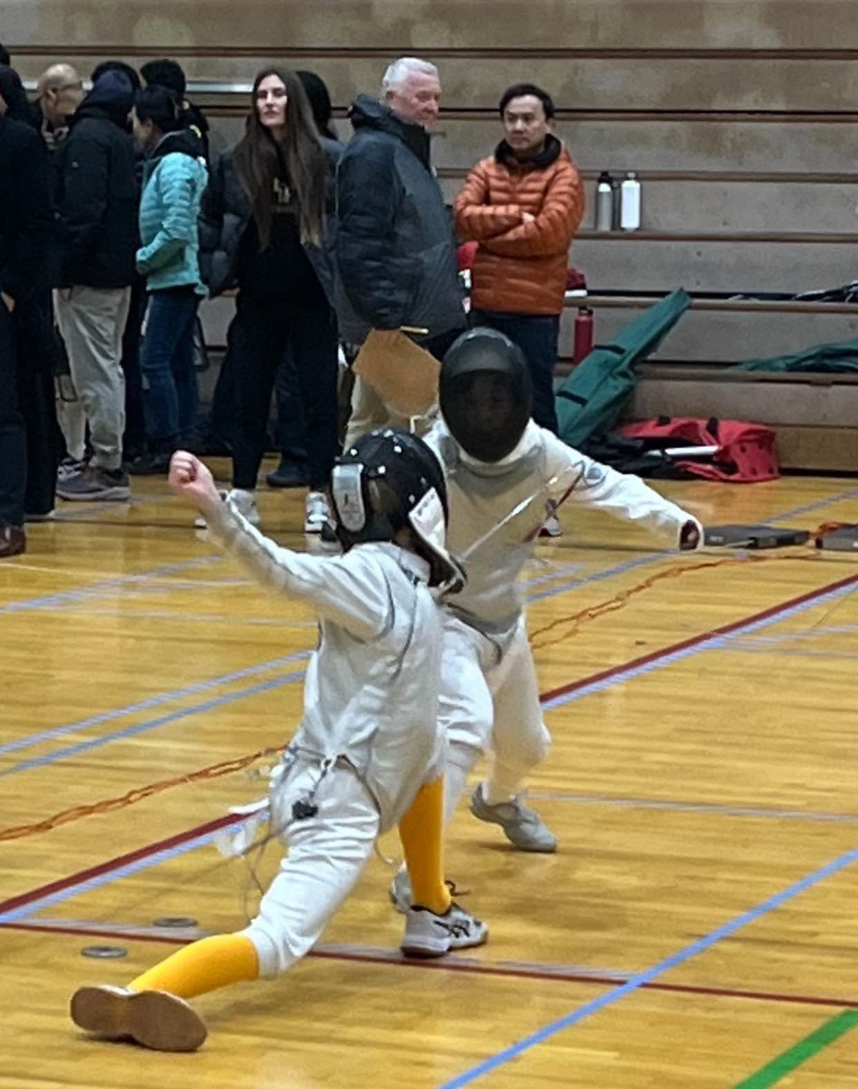 Marin Fencing Academy — A young masked fencer lunging low on a gym floor, watched from the side